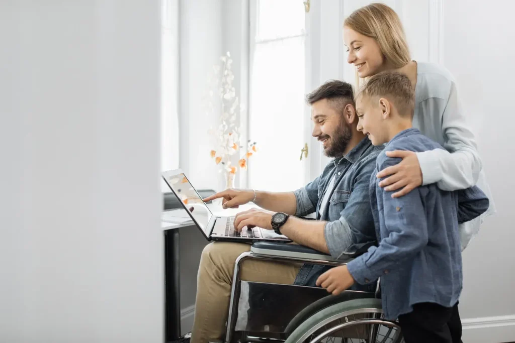 disabled man on wheel chair with his kid and wife looking at laptop and smiling