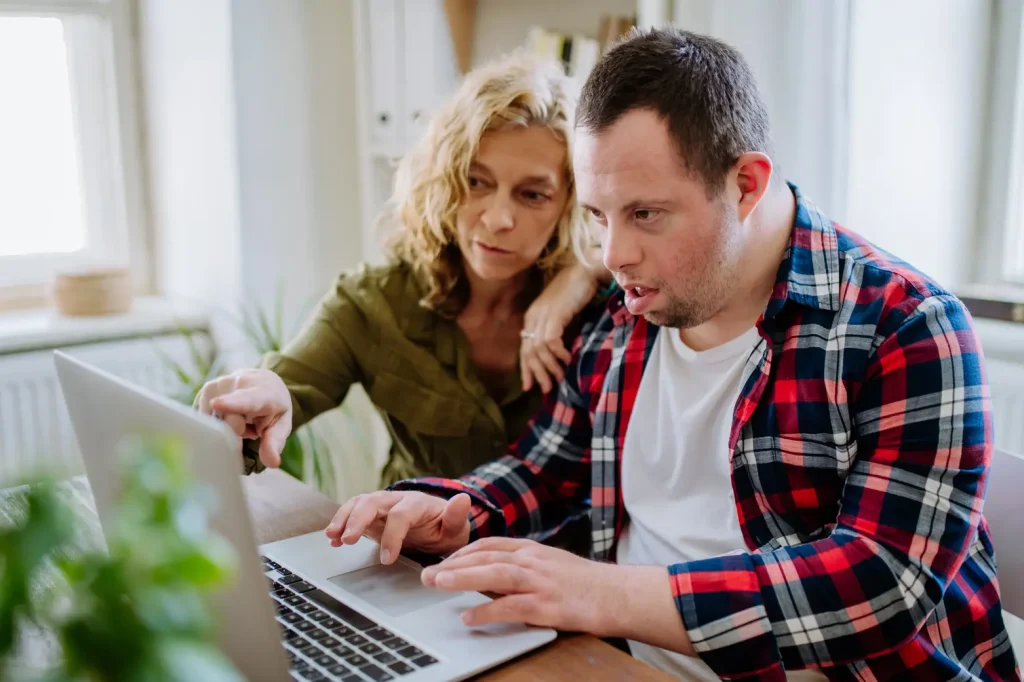 women helping a down syndrome male working on laptop