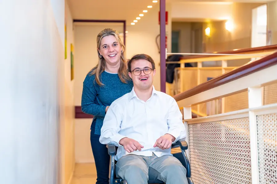 smiling man with a disability and down syndrome on wheel chair with a nurse standing beside him